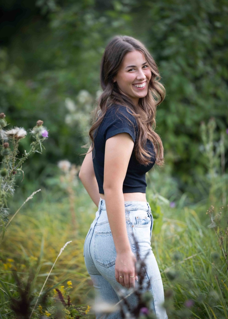 Senior portrait of girl in field with jeans on and a black shirt